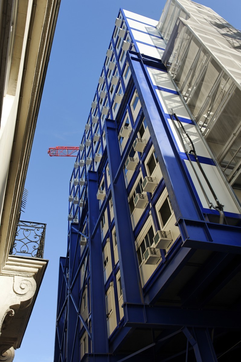 Superposition sur huit étages de bungalow de chantier juxtaposé à une façade d'immeuble dans une rue étroite parisienne. 